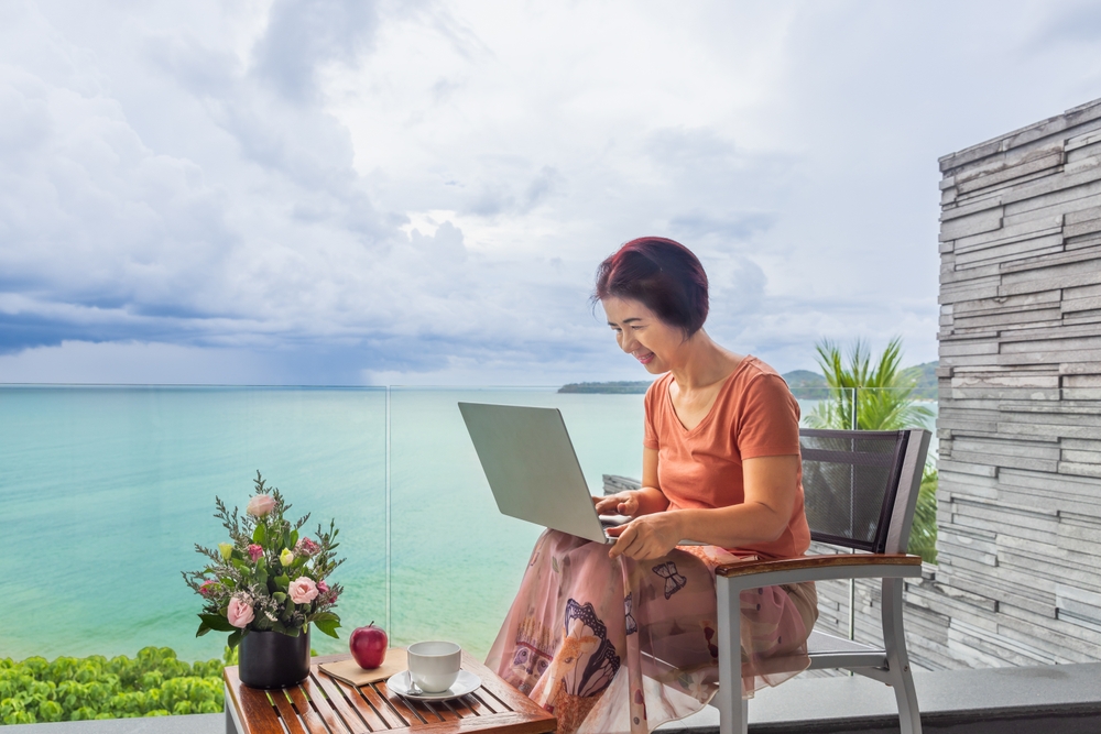 Senior digital nomad woman working at luxury villa in Phuket. andaman sea as background.