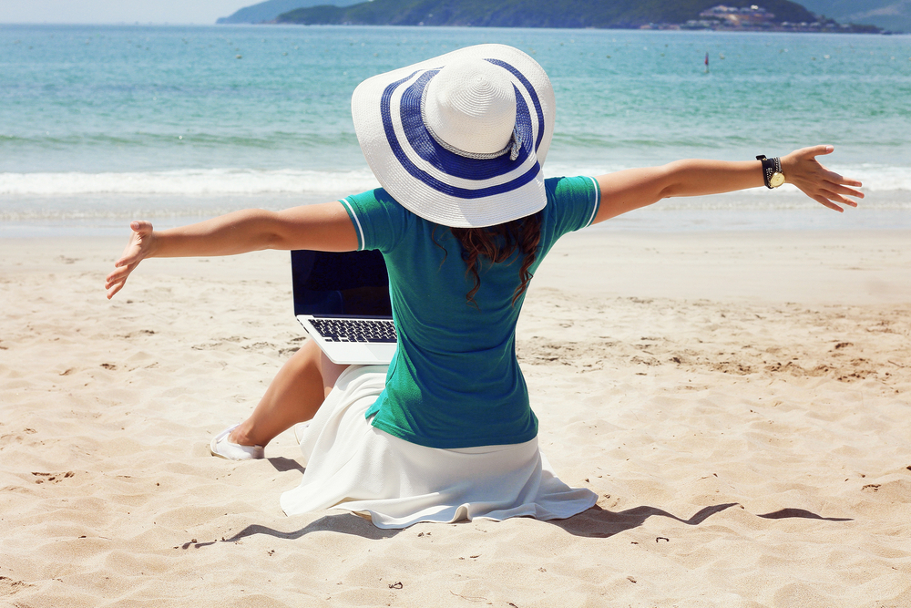 Beautiful woman with a bag working on laptop computer at beach